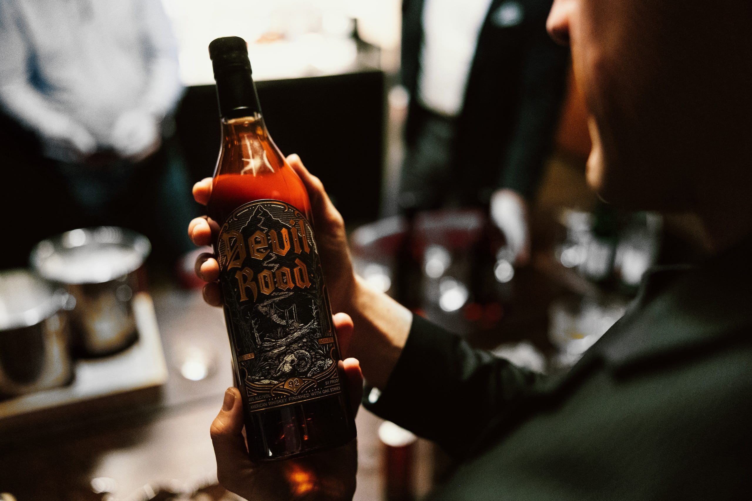 Man in a black suit holding a bottle of Devil Road American Whiskey by Hell & Heaven Spirits